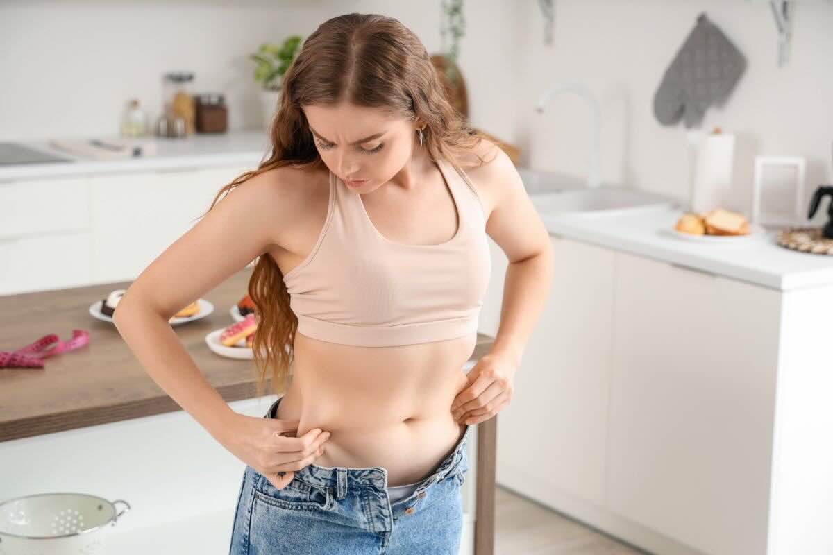 Ragazza che cerca di chiudere jeans, grasso addominale